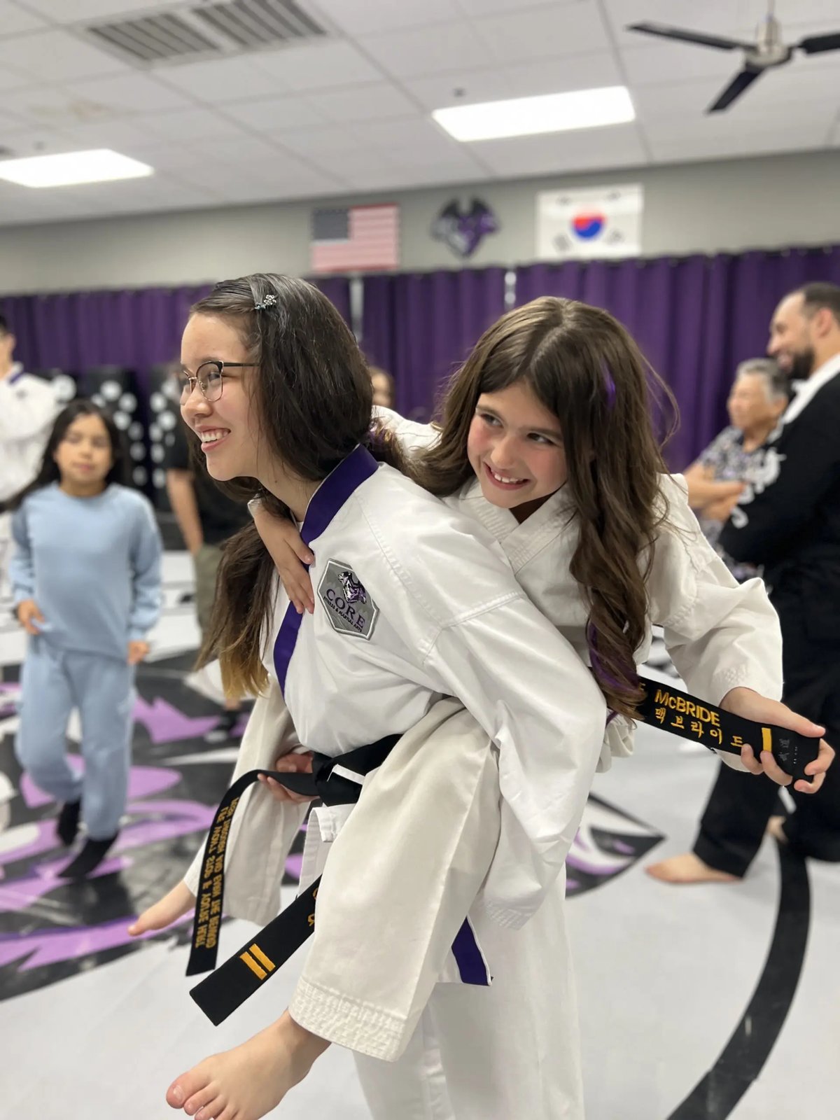 Two black-belt students laughing during a piggyback moment at CORE Fitness & Martial Arts in Henderson
