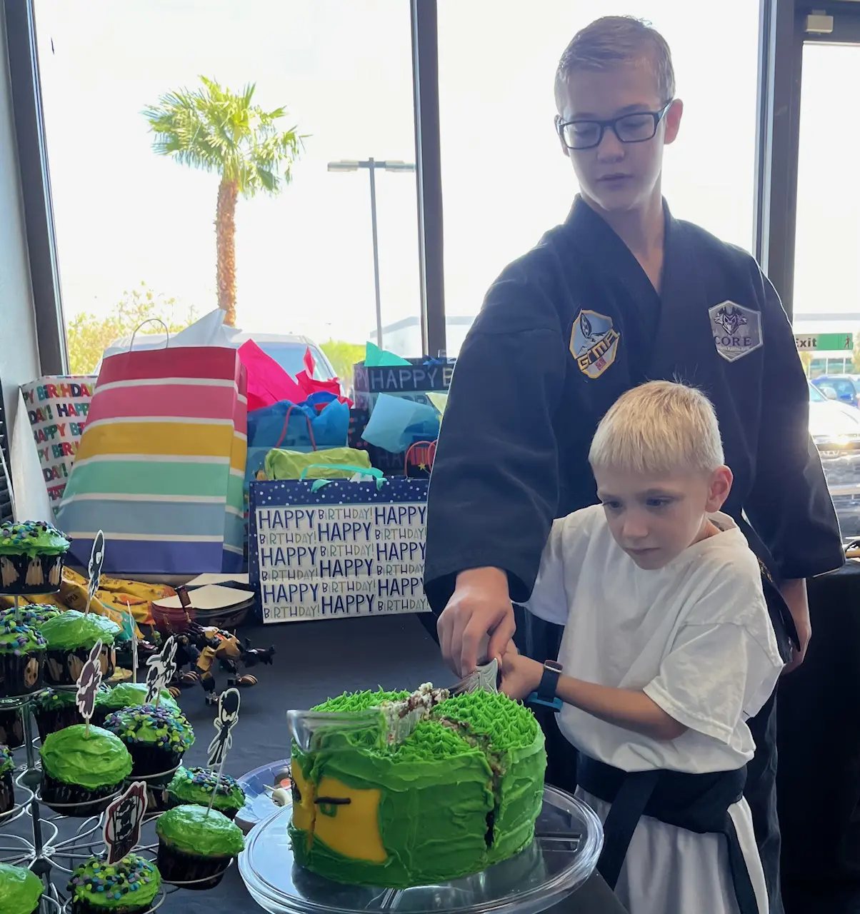 A birthday boy cutting his ninja cake with a black-belt coach at CORE Fitness & Martial Arts in Henderson