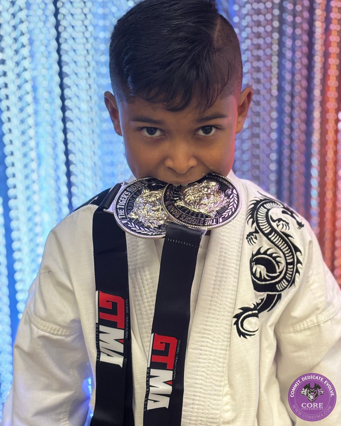A proud student biting his competition medals at CORE Fitness & Martial Arts in Henderson