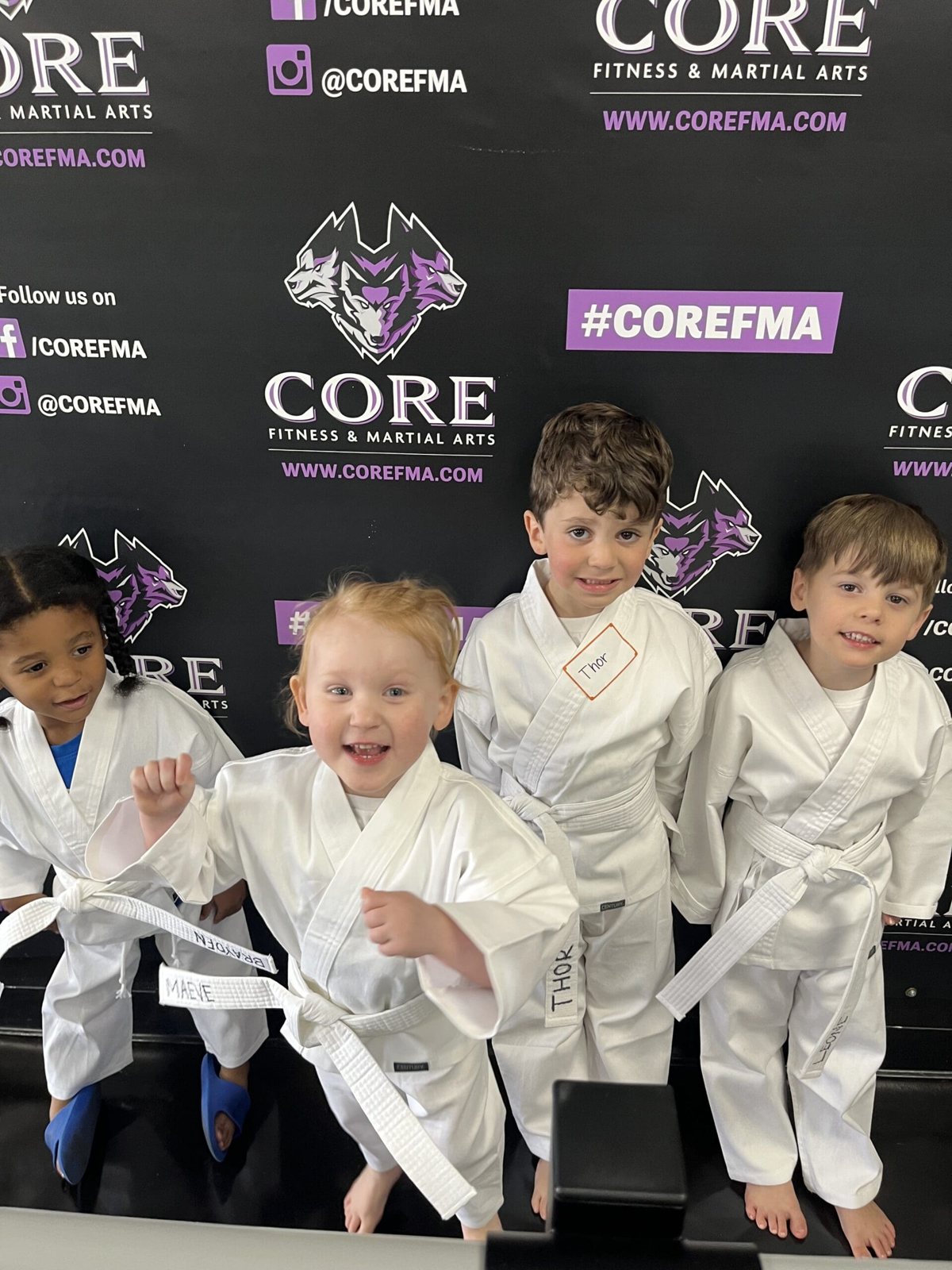 Smiling Wolf Pups in white uniforms in front of the CORE wall at CORE Fitness & Martial Arts in Henderson