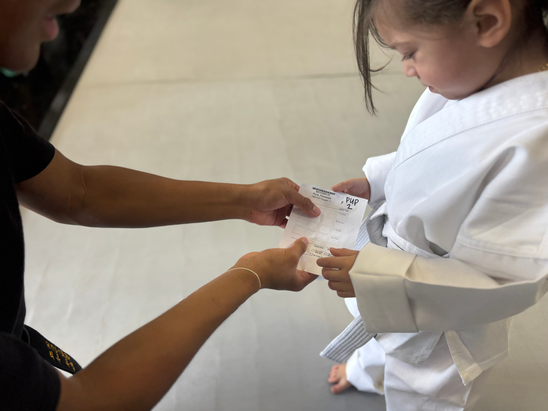 An instructor handing a young Wolf Pup her stripe card at CORE Fitness & Martial Arts in Henderson